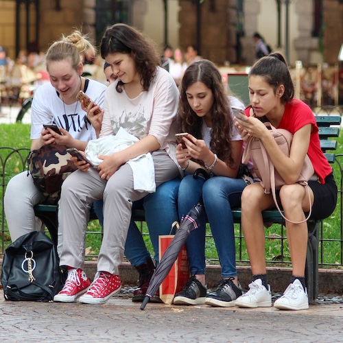 Four teenagers on a bench using their mobile phones without anxiety
